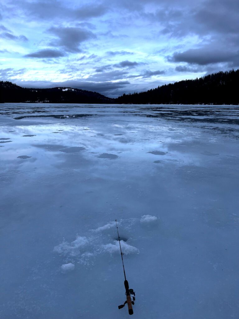 fishing pole sitting by an ice hole on a frozen lake