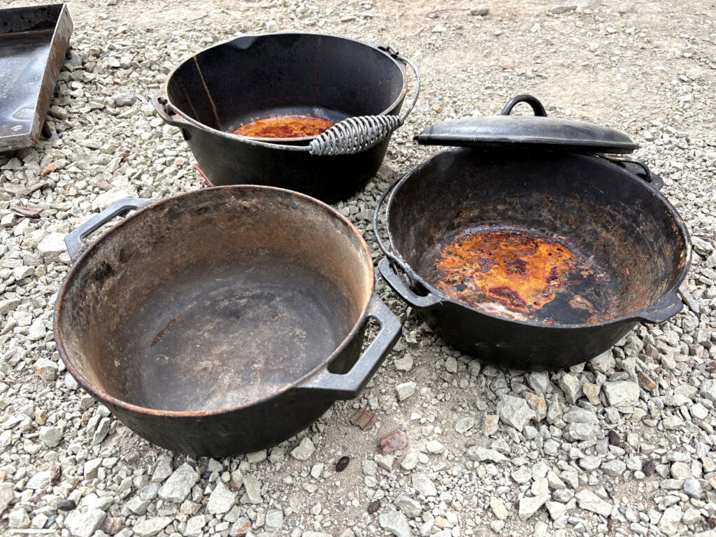Rusty dutch ovens sitting on the ground outside.